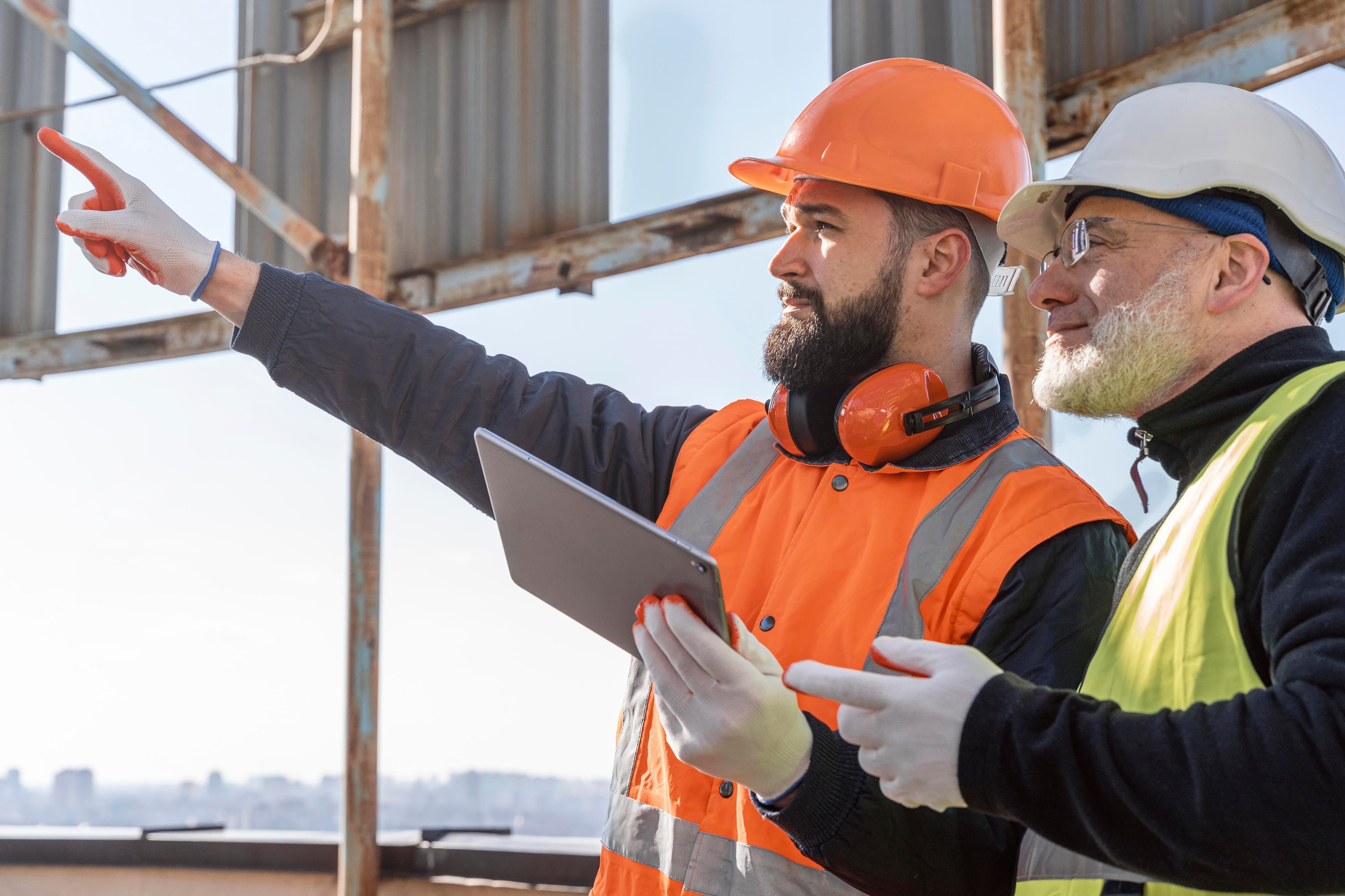 Two energy professionals in hard hats reviewing plans on a laptop at an industrial site