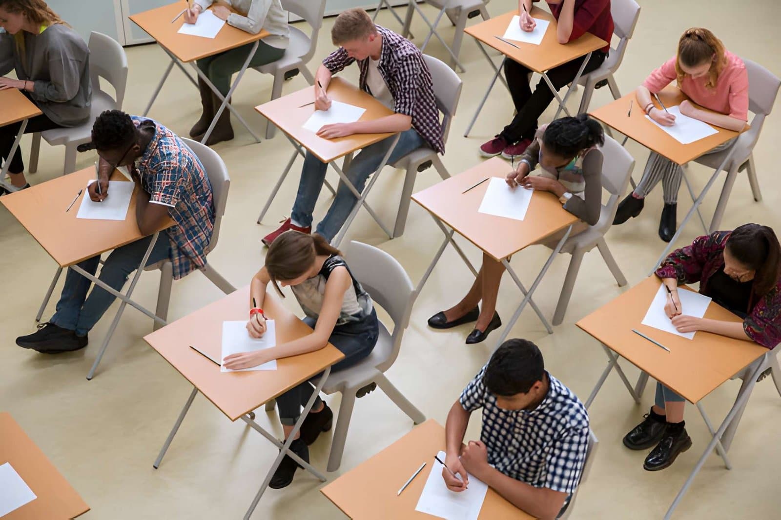 Students sitting exams at individual desks in a classroom, writing on papers during GCSE results season